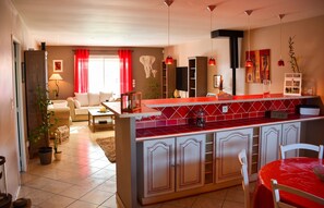 A modern kitchen with a red countertop, white cabinets, and a dining area with a red table and chairs. - Homerez - Villa in Carcassonne (Carcassonne)