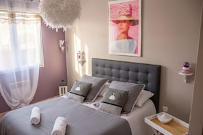 A bedroom with a tufted headboard, a bed with grey bedding and decorative pillows, a bedside table with a lamp, and a framed picture on the wall. - Homerez - Villa in Carcassonne (Carcassonne)