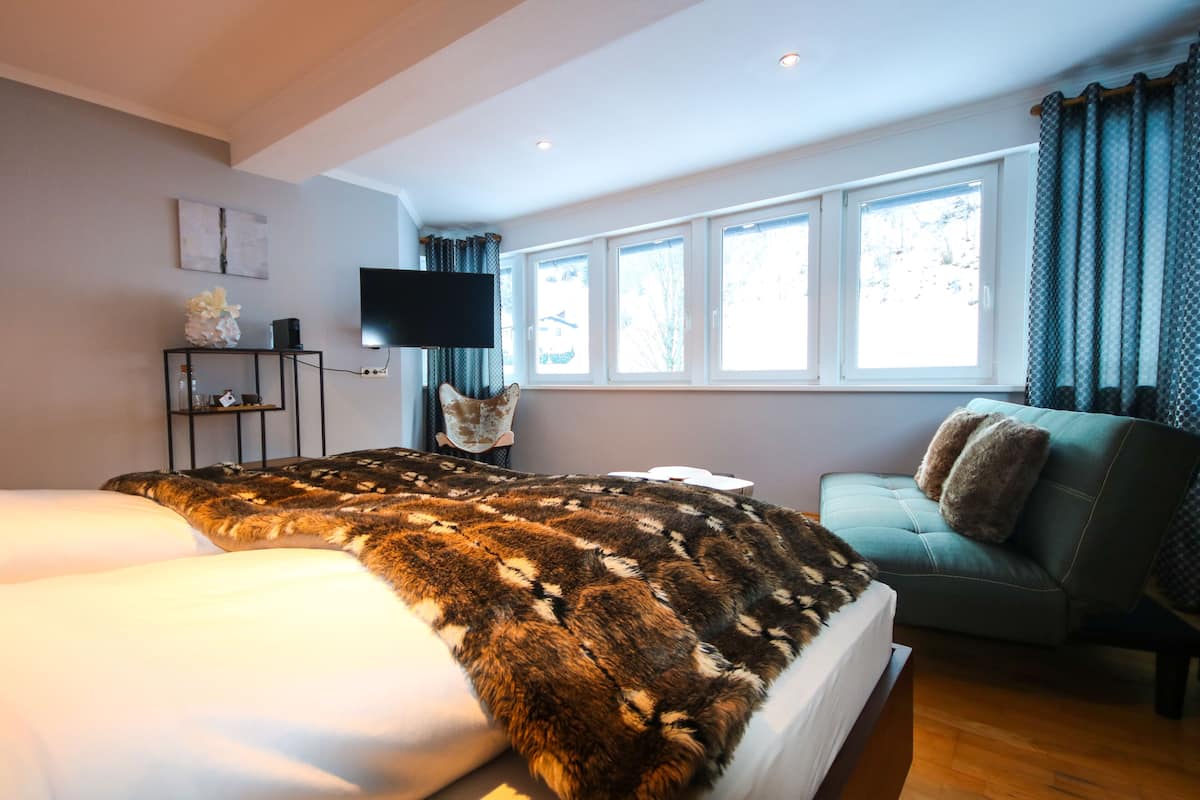 A modern hotel room with a large bed, a sofa, a flat-screen TV, and a window with curtains.