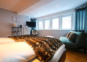 A modern hotel room with a large bed, a sofa, a flat-screen TV, and a window with curtains. - Appartement Bosek (Wagrain)