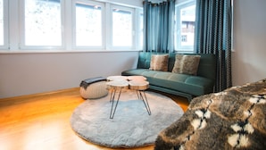 A living room with a sofa, a round rug, a coffee table, and a window with curtains. - Appartement Bosek (Wagrain)