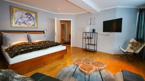 A bedroom with a large bed, a TV, a chair, and a painting on the wall. - Appartement Bosek (Wagrain)