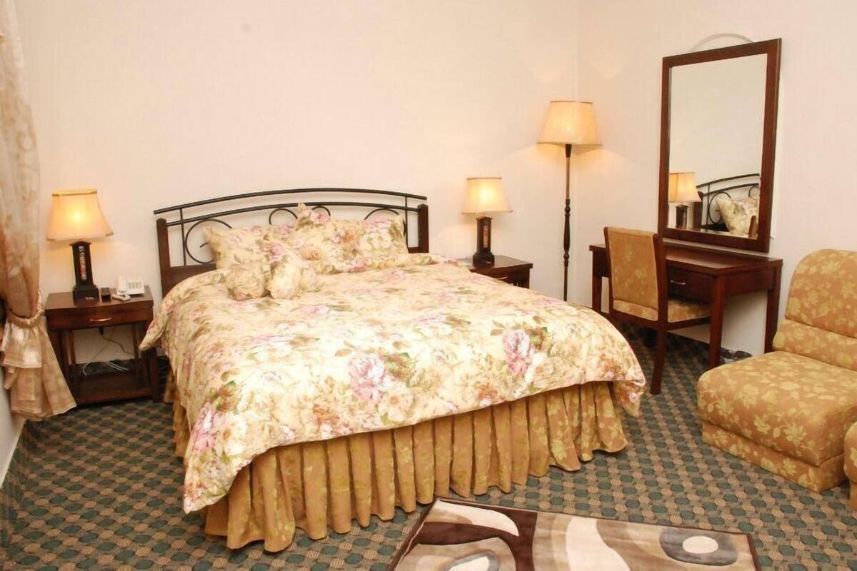 A bedroom with a bed, two bedside tables with lamps, a chair, a desk, and a mirror.