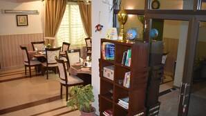 A dining area with a table and chairs, a bookshelf with books, a potted plant, and a fire extinguisher. - Savoy Inn (Islamabad)