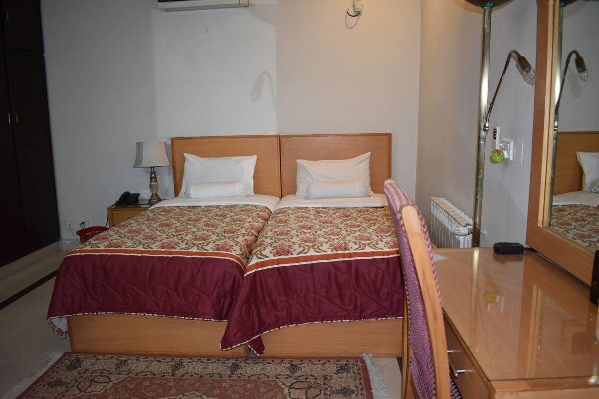 A double bed with a patterned bedspread, a bedside table with a lamp, and a mirror reflecting the room.