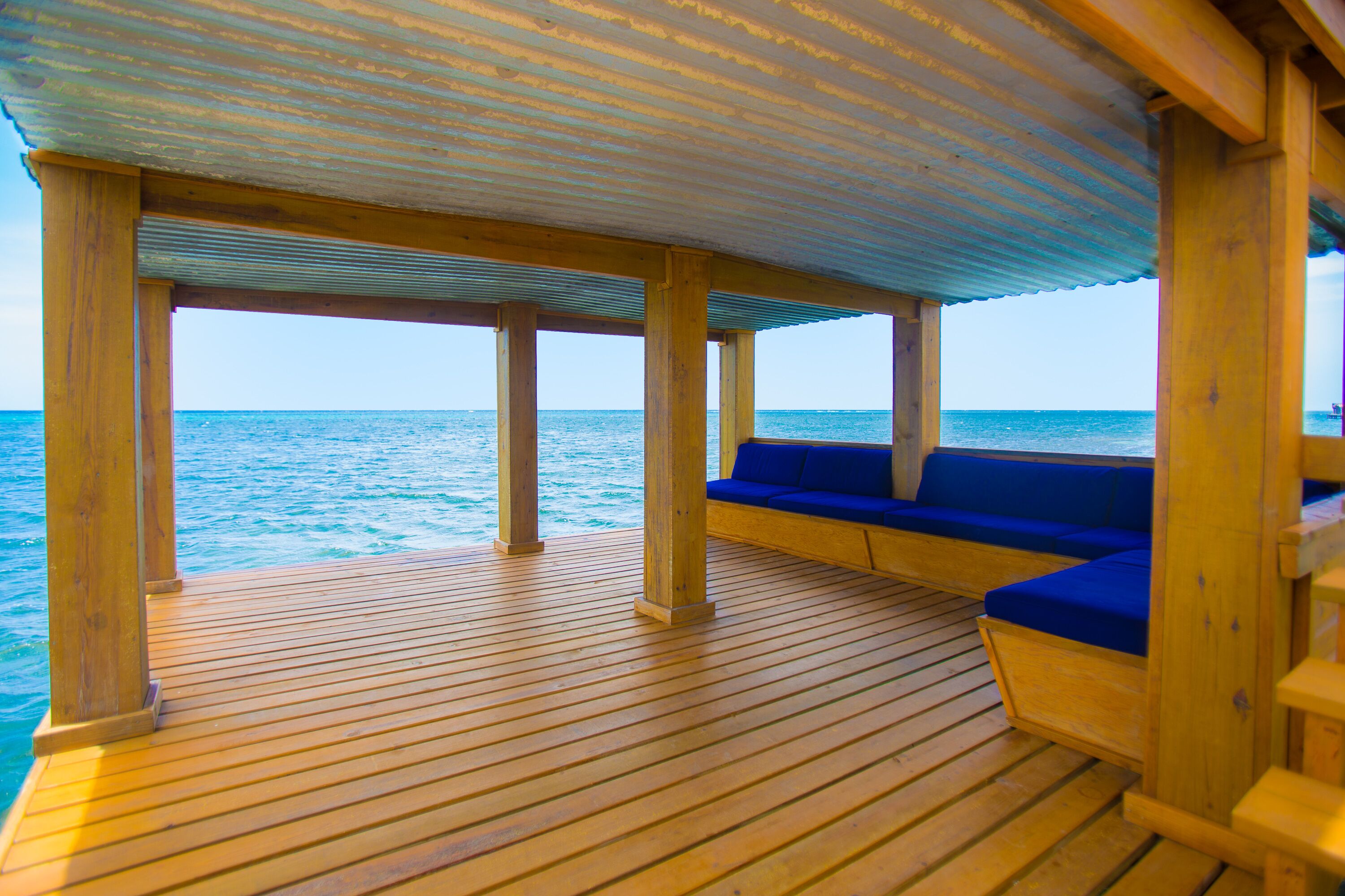 A wooden deck with a blue cushioned seating area overlooking the ocean.