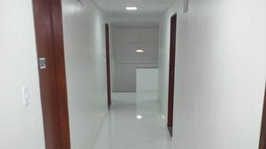 A corridor with white tiled floors and wooden doors, leading to a room with a white wall and a light fixture. - Requinte Hotel Itabuna (Itabuna)