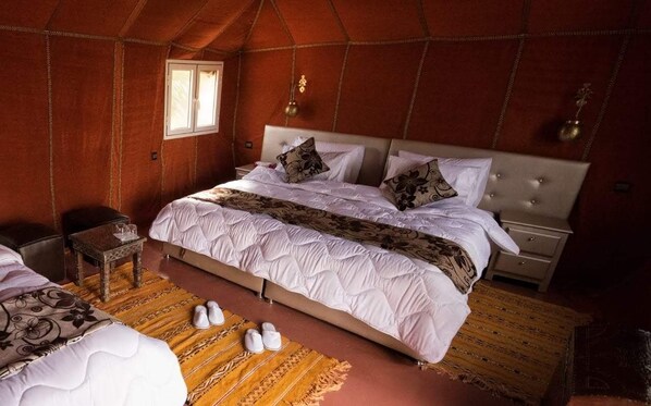 A spacious tent-style room with a large bed, a small table, and a window.