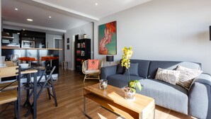 A modern living room with a grey sofa, wooden coffee table, and a dining area with a wooden table and chairs.