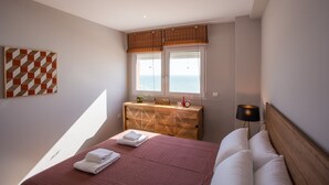 A bedroom with a bed, a wooden dresser, a window with a view, and a wall-mounted artwork.