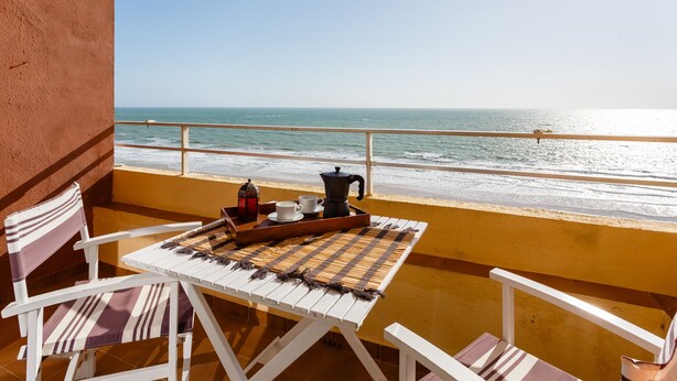 A balcony with a table set for two, overlooking a beach.