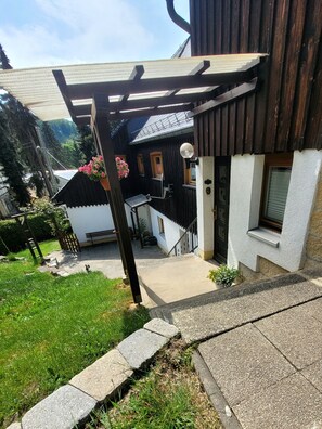 Una casa con fachada de madera, un porche con banca y un pequeño jardín.