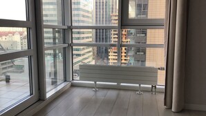 A room with a large window, a wooden floor, and a white bench. - Green Wood Apartments Platinum Towers (Warsaw)