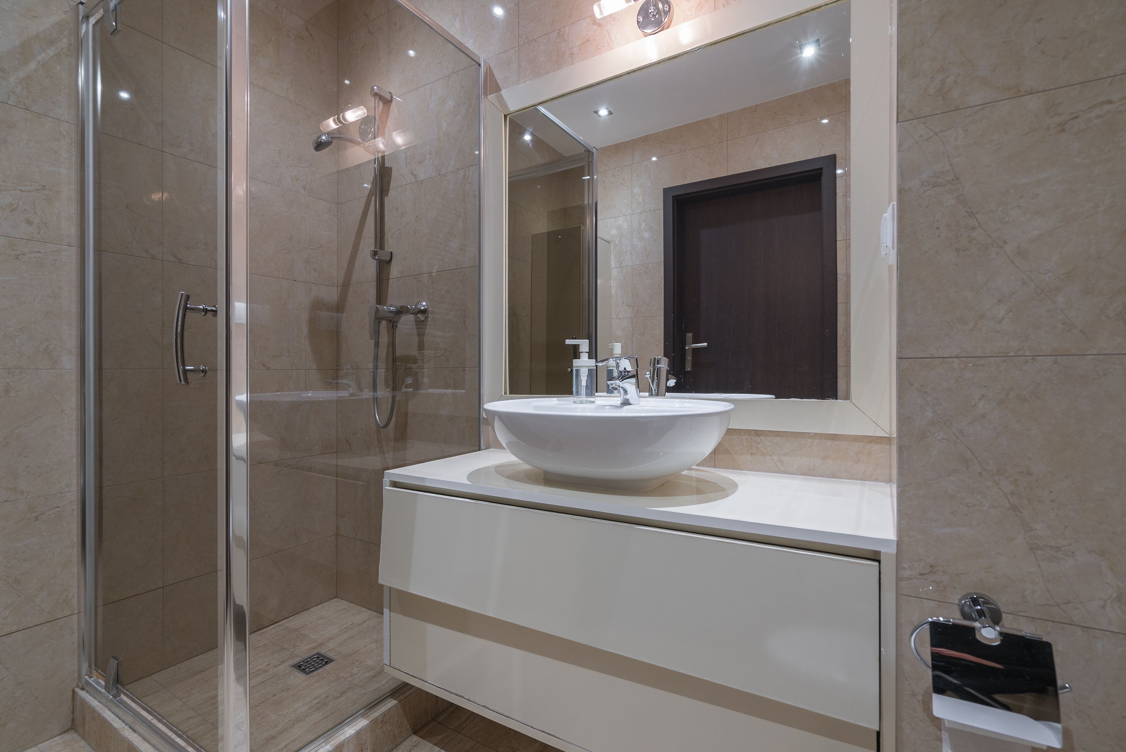 Un baño moderno con cabina de ducha de vidrio, un lavabo blanco con un espejo grande encima y una puerta oscura.