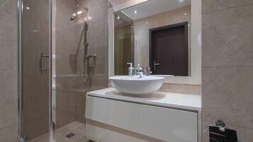Un baño moderno con cabina de ducha de vidrio, un lavabo blanco con un espejo grande encima y una puerta oscura.