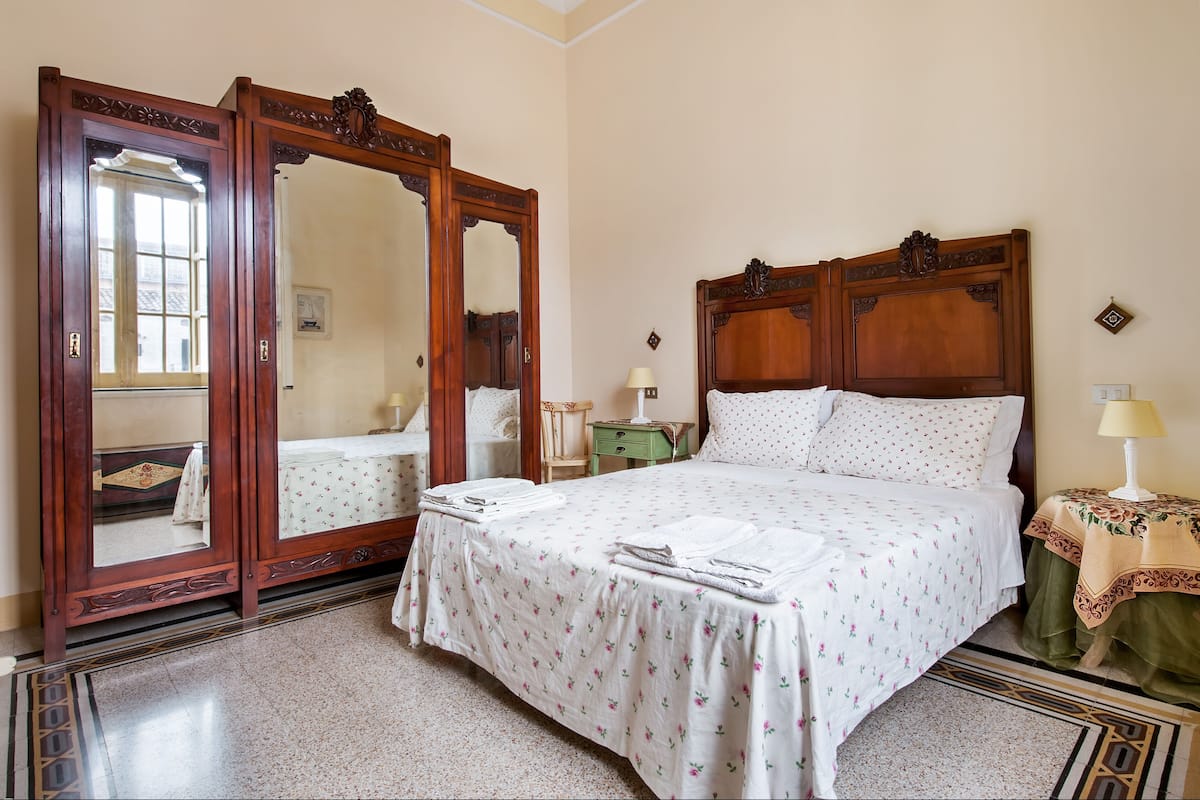 A bedroom with a large wooden bed, a matching wardrobe, a bedside table with a lamp, and a small table with a lamp.