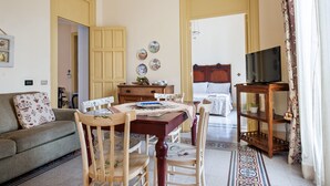 A cozy living room with a sofa, dining table, chairs, a TV stand, and a bed with a headboard. - La Casa di Zoe (Palermo)