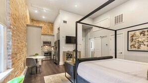 A modern bedroom with a four-poster bed, a dining area with a table and chairs, and a kitchen in the background. - WHERE GLAM MEETS COZY! THE PERFECT PLACE FOR A DOWNTOWN GETAWAY! | The Sazerac (New Orleans)
