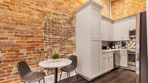 A kitchen with a brick wall, white cabinets, and a round table with two chairs. - WHERE GLAM MEETS COZY! THE PERFECT PLACE FOR A DOWNTOWN GETAWAY! | The Sazerac (New Orleans)