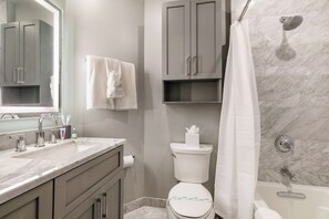 Een badkamer met een marmeren wastafel, toilet, douche met glazen deur en een spiegel.