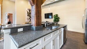 Una cocina con encimeras de granito, gabinetes blancos, un lavamanos de acero inoxidable y lavavajillas integrado.