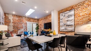 A modern living room with a brick wall, a sofa, a coffee table, and a dining area with chairs and a table.