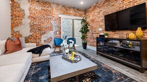 A modern living room with a brick wall, a flat-screen TV, a sofa, a coffee table, and a large window.