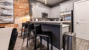 A modern kitchen with white cabinets, a stainless steel refrigerator, and a bar area with black stools.