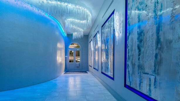 A hallway with a blue-lit floor, a white wall with a blue border, and a door at the end.