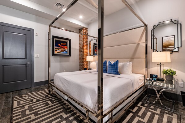 Une chambre d’hôtel moderne avec un lit à baldaquin, un mur décoratif en briques et un grand miroir.
