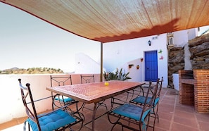 Un portico coperto con tavolo e sedie, una porta blu e un muro in pietra.