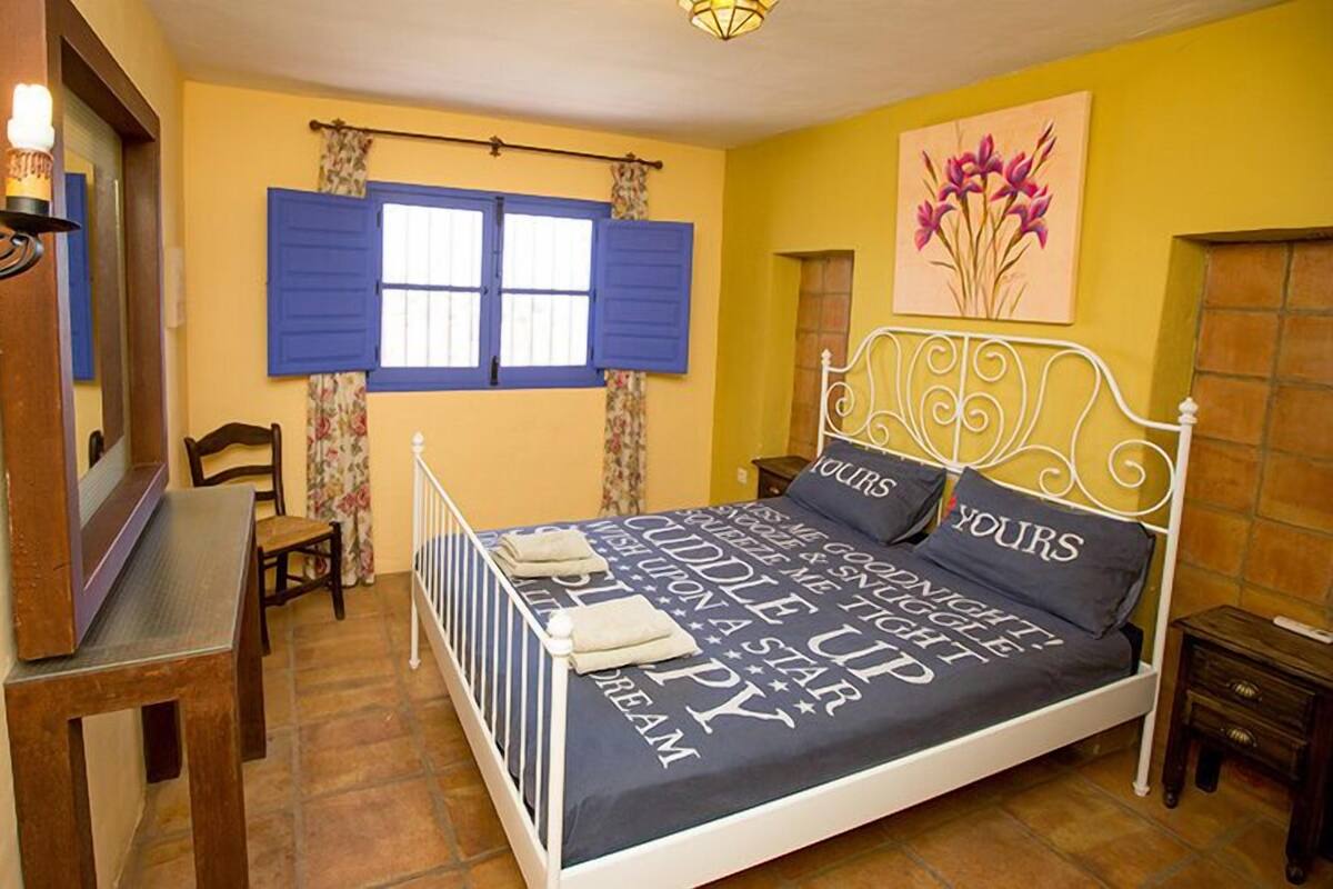 A bedroom with a bed, a desk, a chair, and a window with blue shutters.