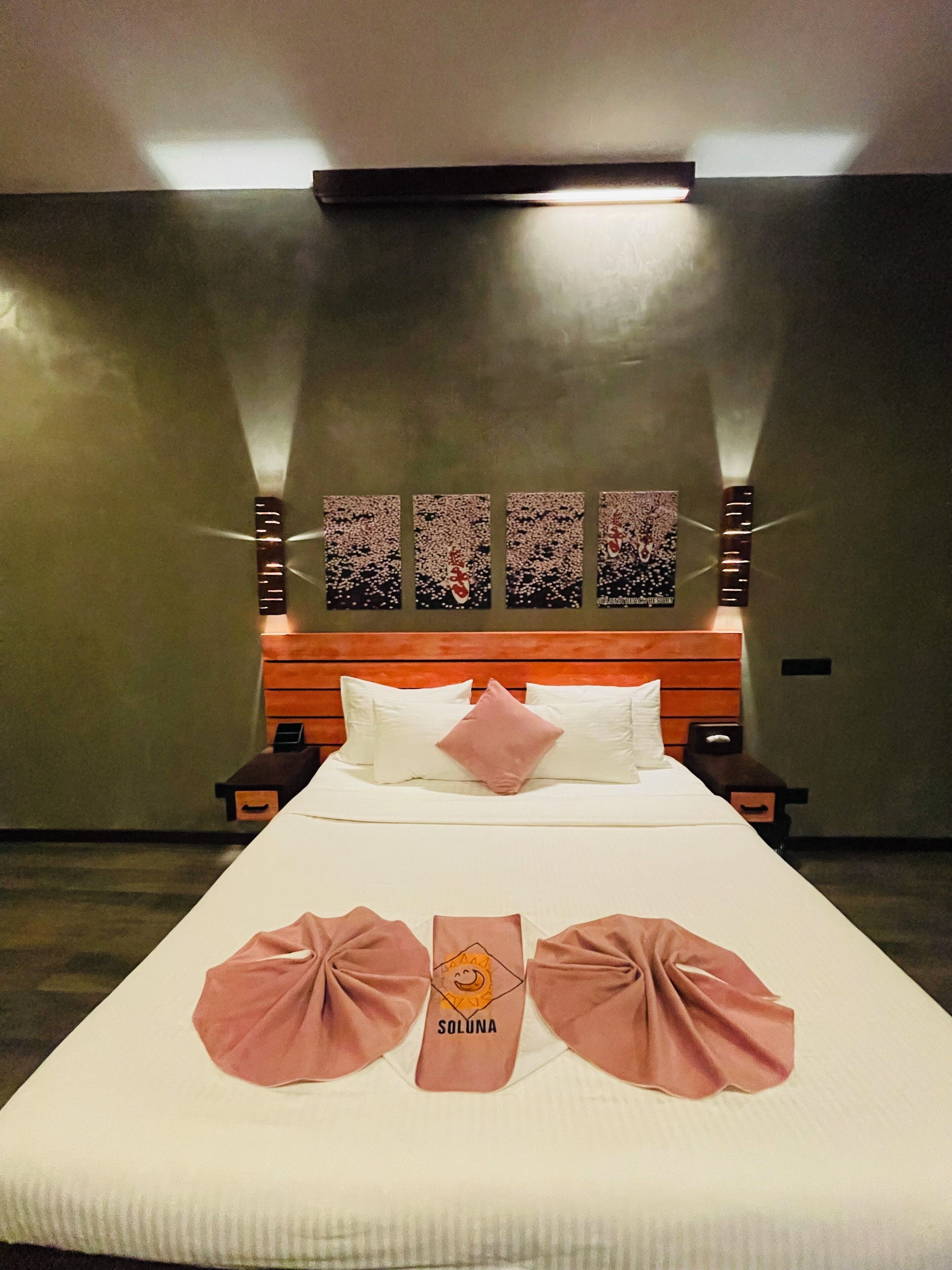 Una habitació d'hotel amb un llit gran, un reposacapses de fusta i tres quadres penjats a la paret.