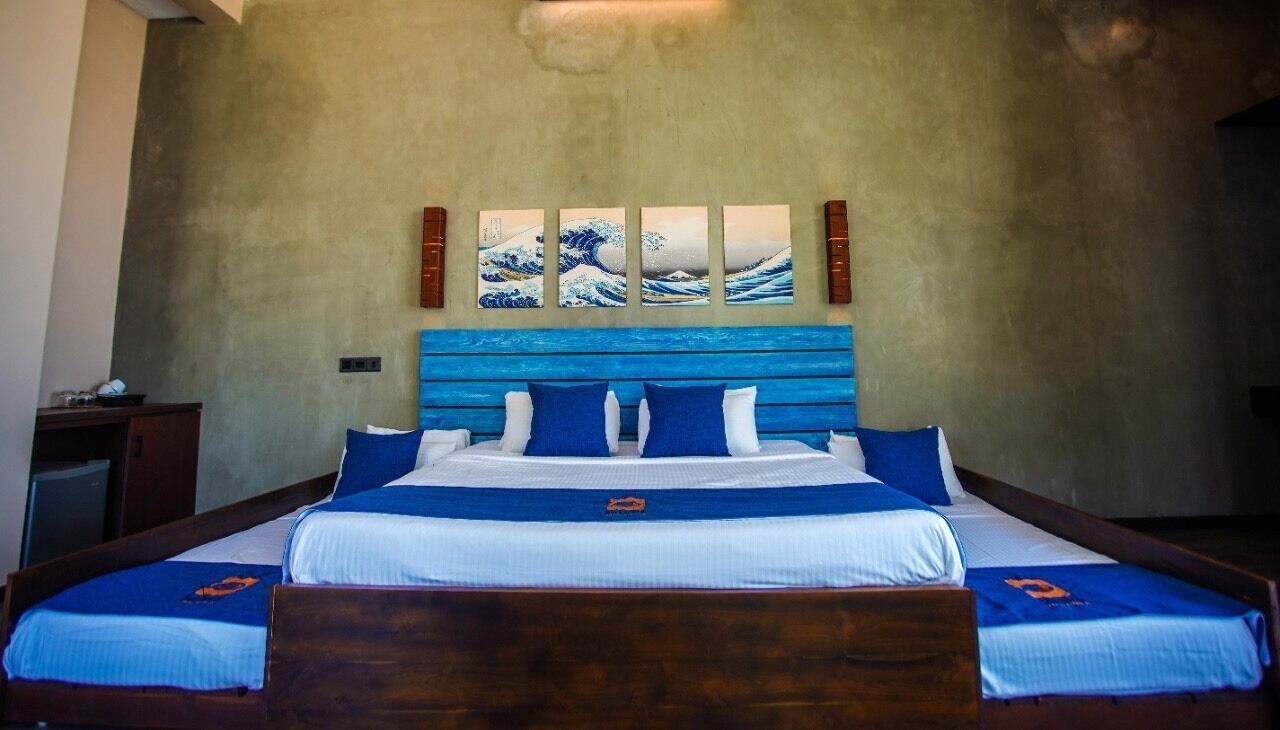 A bed with a blue headboard, white bedding, and a blue accent pillow. There are four paintings on the wall above the bed.
