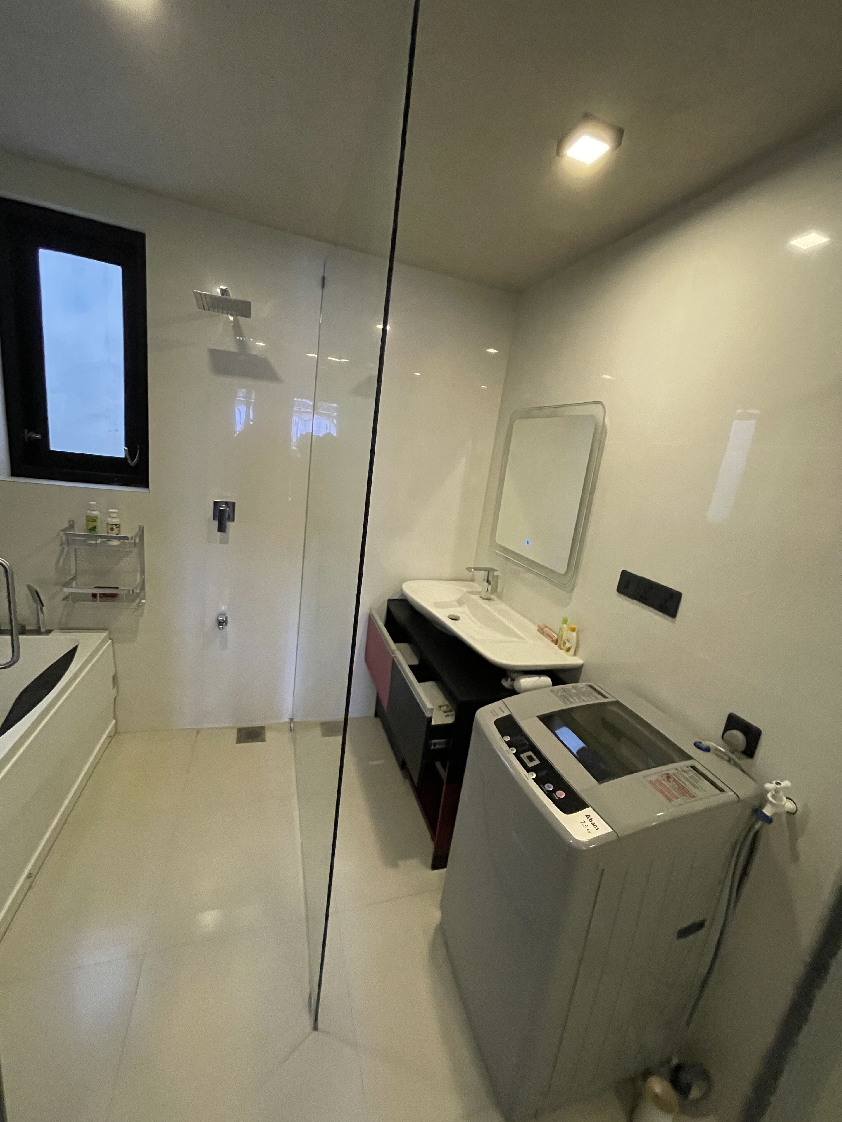 A modern bathroom with a glass partition, a large mirror, a sink, and a hairdryer.