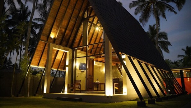 Un edificio moderno de forma triangular con grandes ventanales y vigas de madera, rodeado de palmeras.