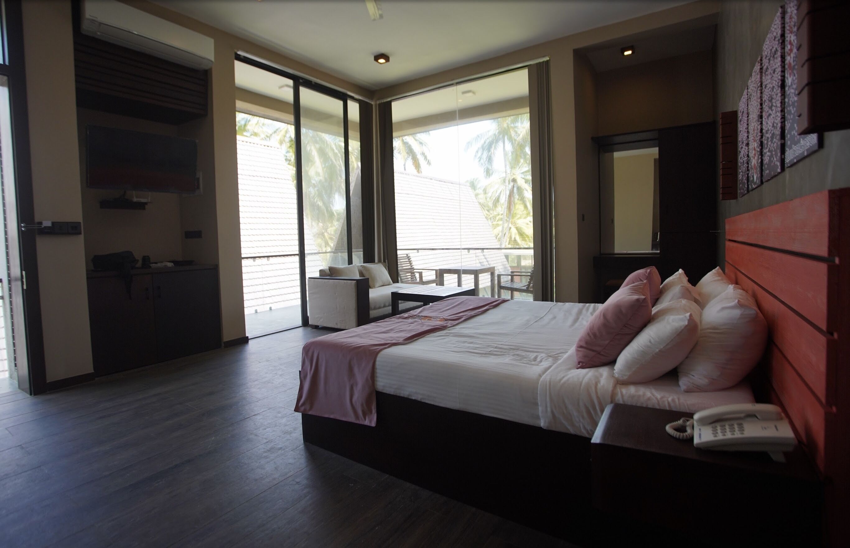 Una habitación de hotel moderna con una cama grande, un teléfono en la mesita de noche y vistas a palmeras a través de puertas correderas de vidrio.