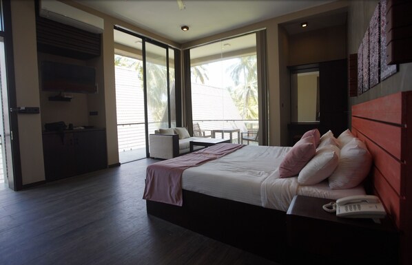 Una habitación de hotel moderna con una cama grande, un teléfono en la mesita de noche y vistas a palmeras a través de puertas correderas de vidrio.