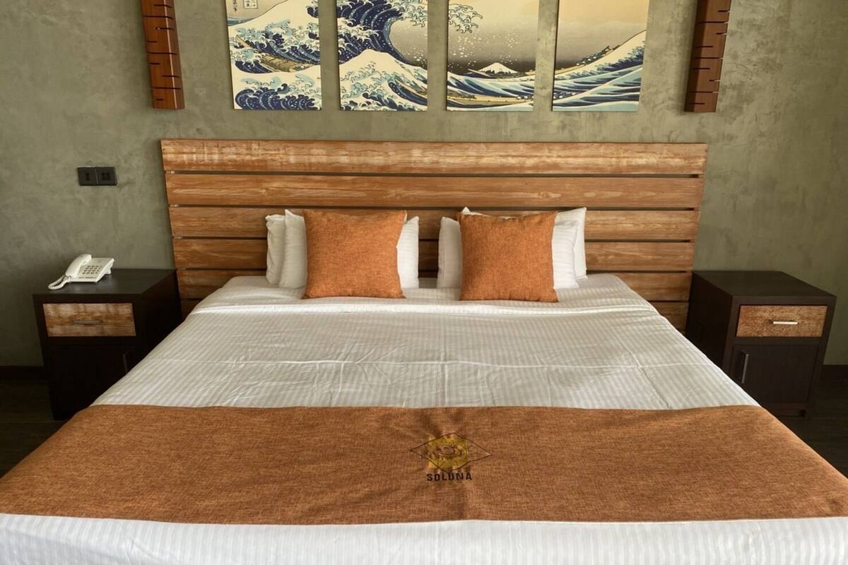A hotel room with a large bed, wooden headboard, two nightstands, and a wall-mounted artwork.