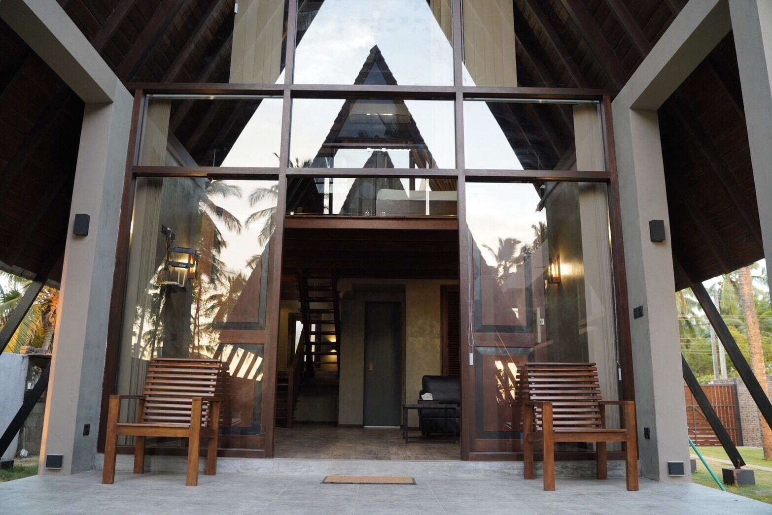 A modern building with a glass facade, wooden benches outside, and a visible interior with a staircase.