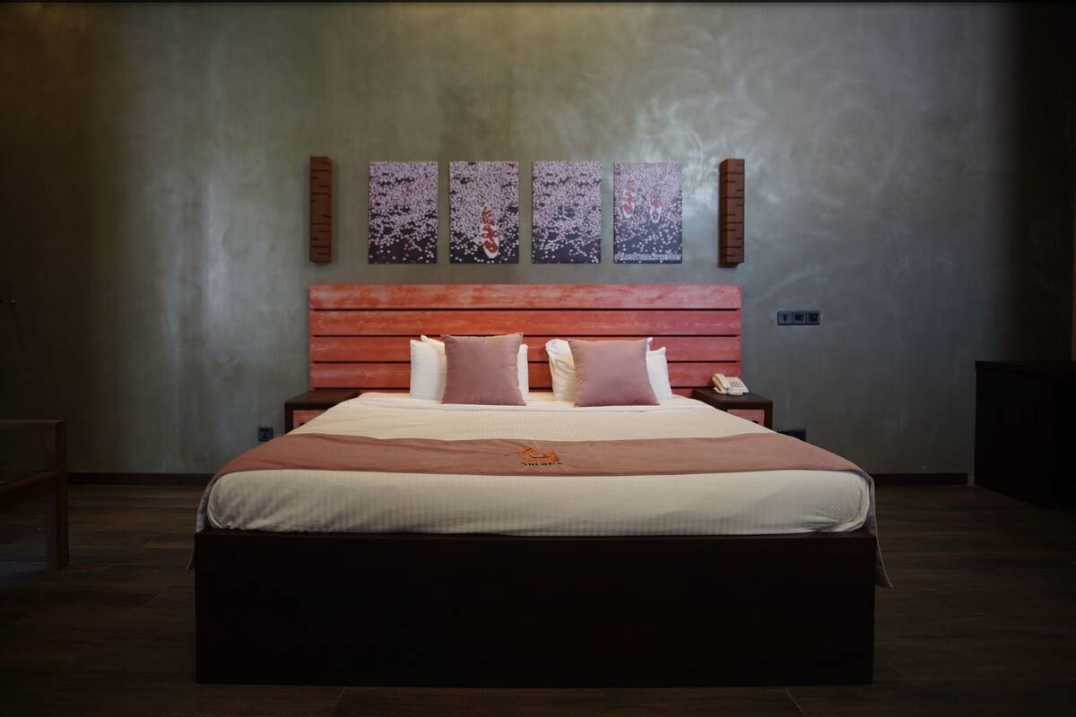 A large bed with a wooden headboard, two bedside tables, and a wall-mounted phone.