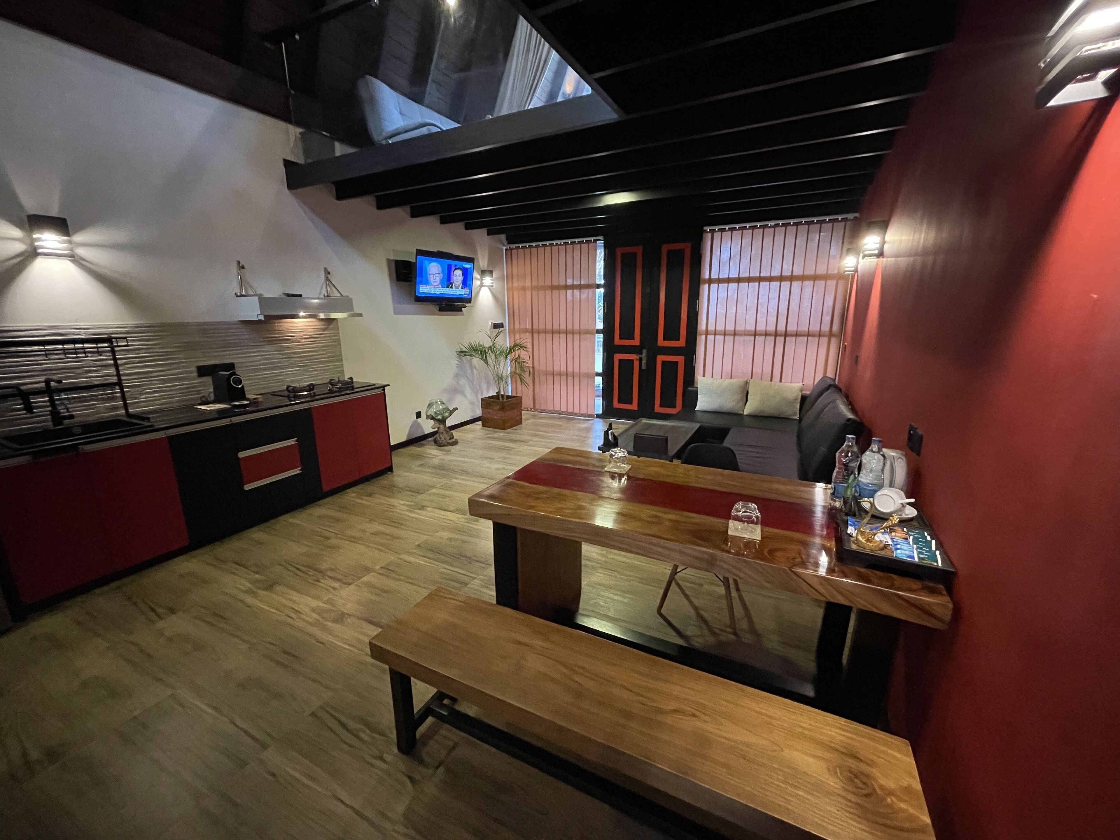 A modern kitchen with a wooden countertop, a bench, and a dining table. There is a TV mounted on the wall and a plant on the floor.
