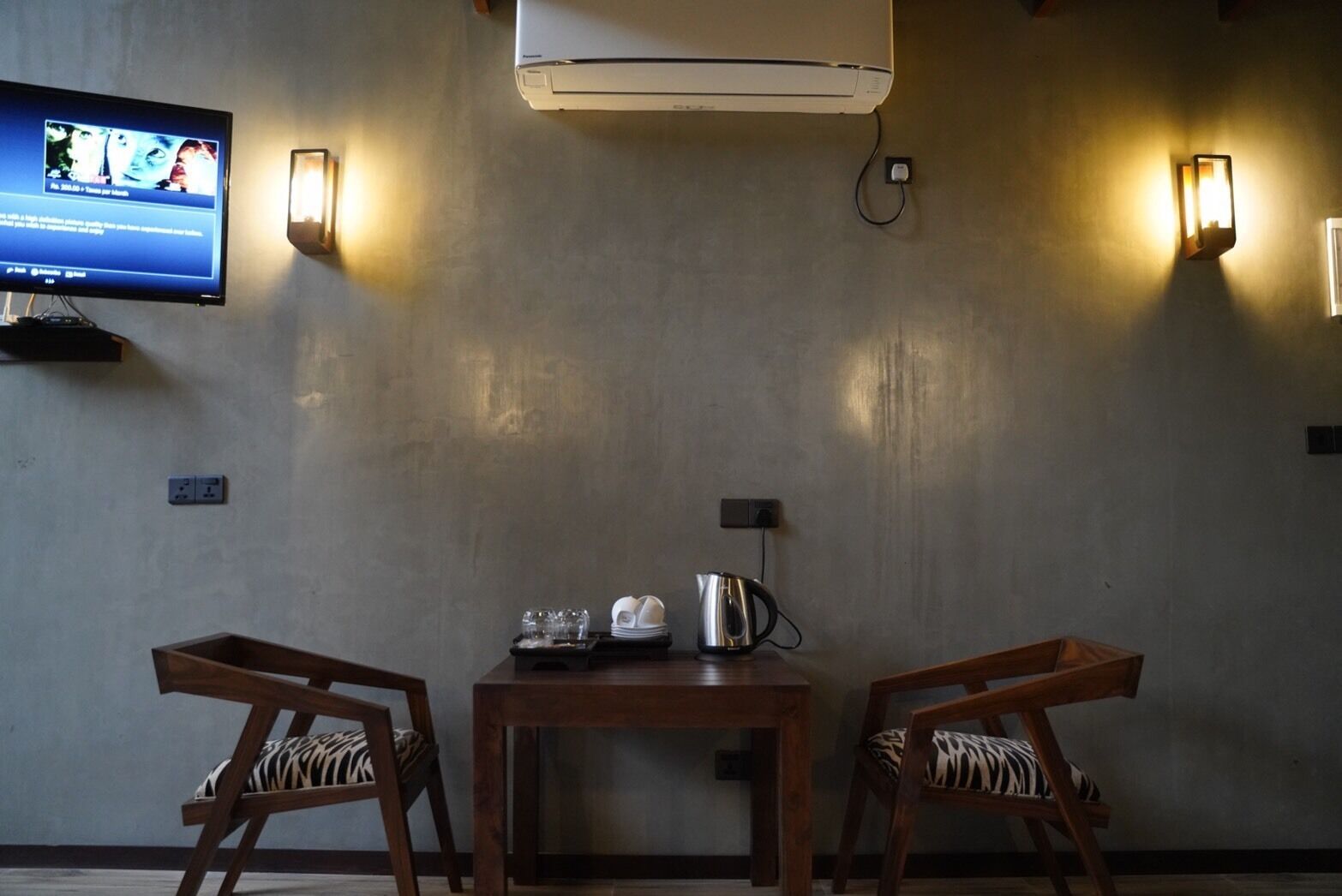 A room with a TV mounted on the wall, a table with chairs, and a coffee maker.