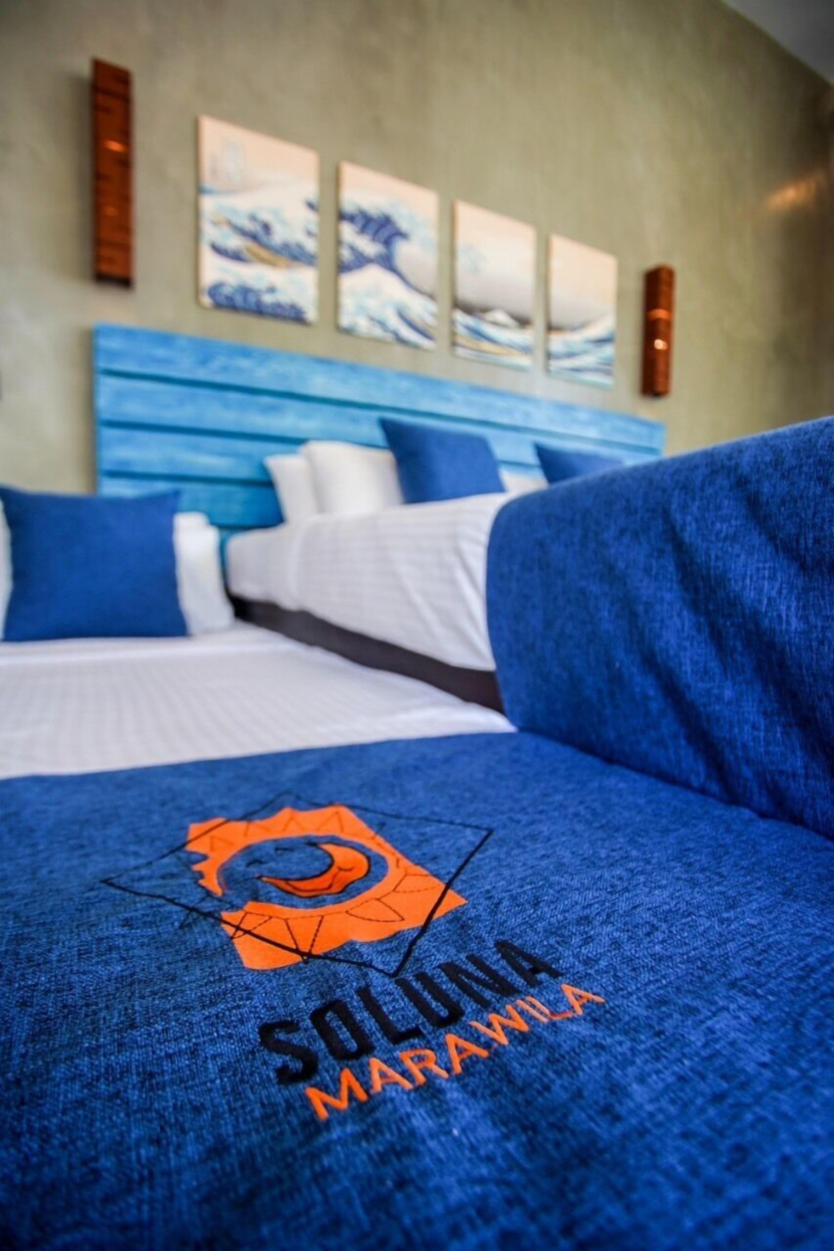 A hotel room with a bed, blue and white bedding, and a logo on the bedspread.