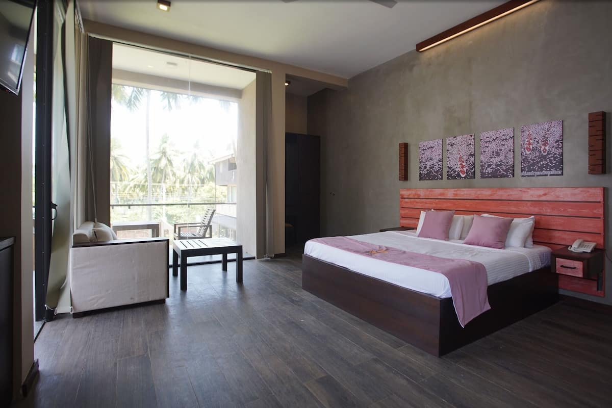 A modern bedroom with a large bed, a bedside table, a chair, and a view of palm trees through the window.