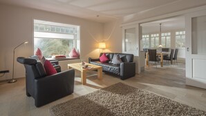 Ein modernes Wohnzimmer mit einer Couch, einem Couchtisch und einer Lampe. Durch einen offenen Durchgang ist ein Essbereich sichtbar.