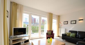 A living room with a TV, a sofa, a red armchair, and a coffee table. - Kapitänshaus Tordalk (Norderney)