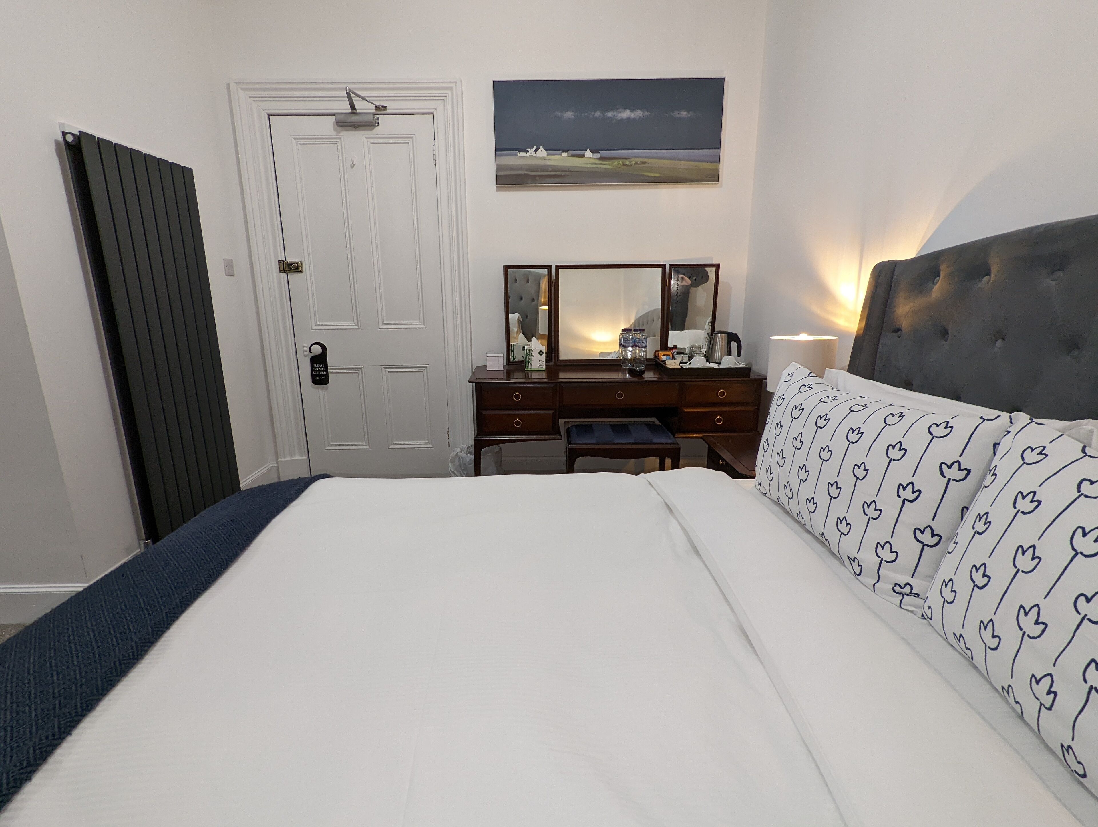 A bedroom with a bed, a dresser, a mirror, and a painting on the wall.