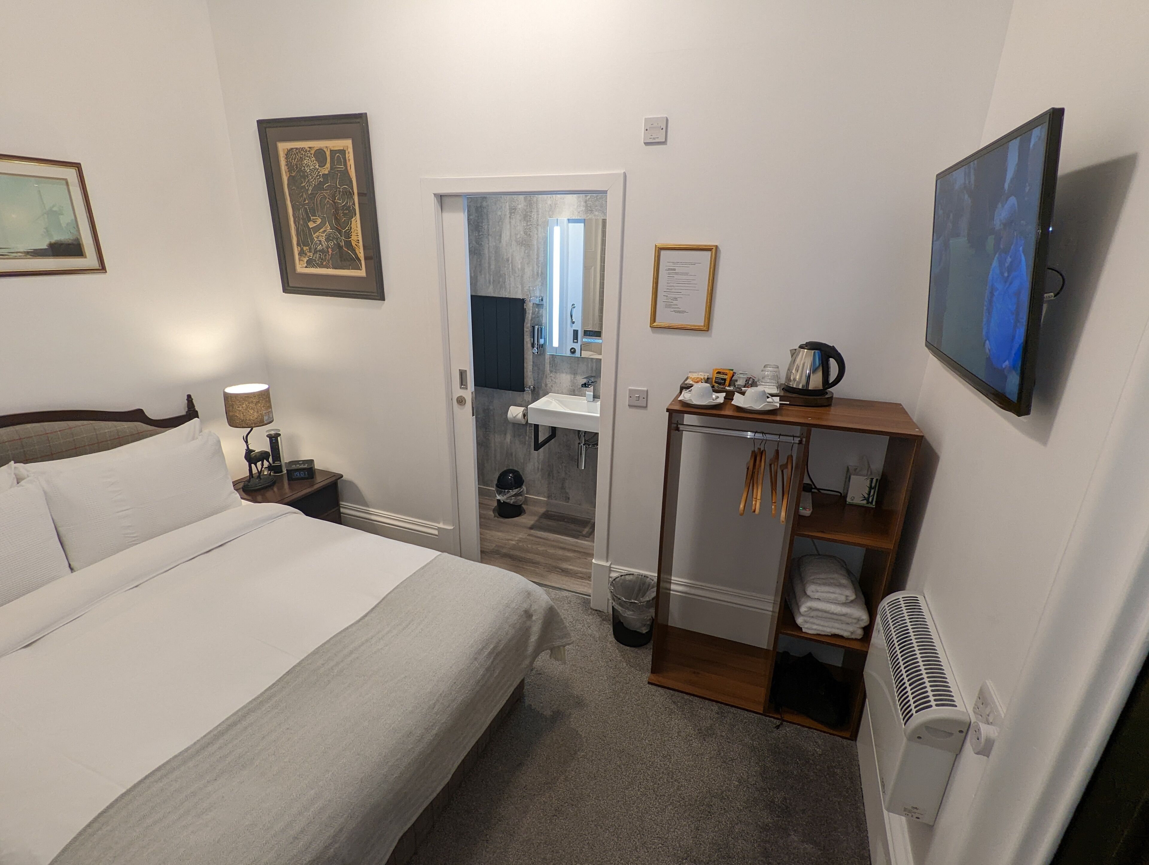 Ein Hotelzimmer mit Bett, Schreibtisch mit Wasserkocher, Fernseher und einem durchgegangenen Tür zu sehendem Badezimmer.