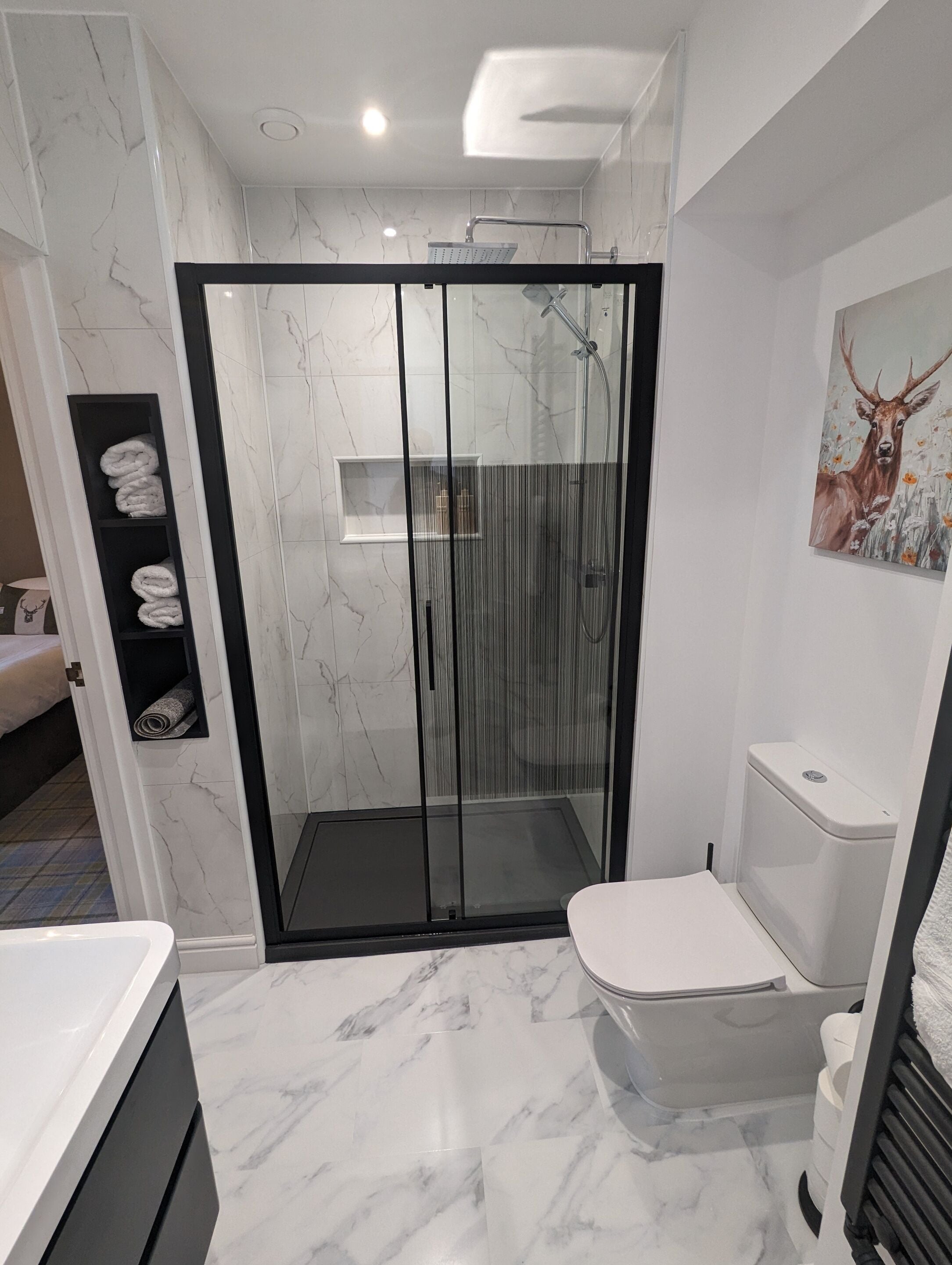 Un baño moderno con ducha envuelta en vidrio, inodoro y un perchero con toallas dobladas cuidadosamente.
